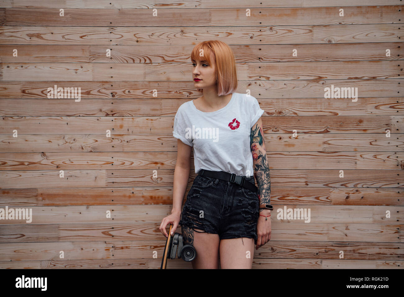 Young woman standing at wooden wall with skateboard Stock Photo