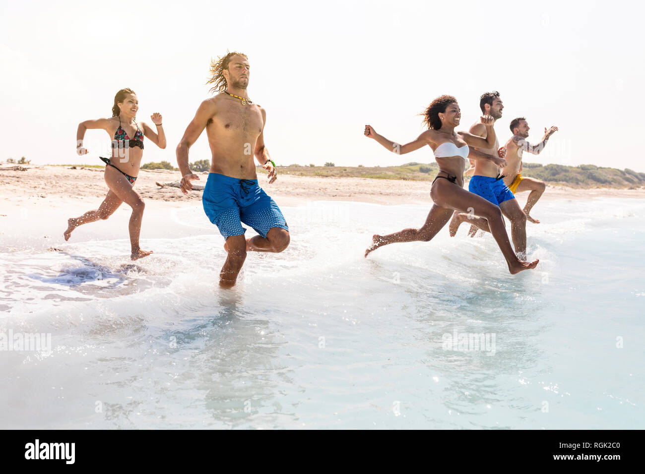 Group of friends having fun on the beach, running into the water Stock Photo