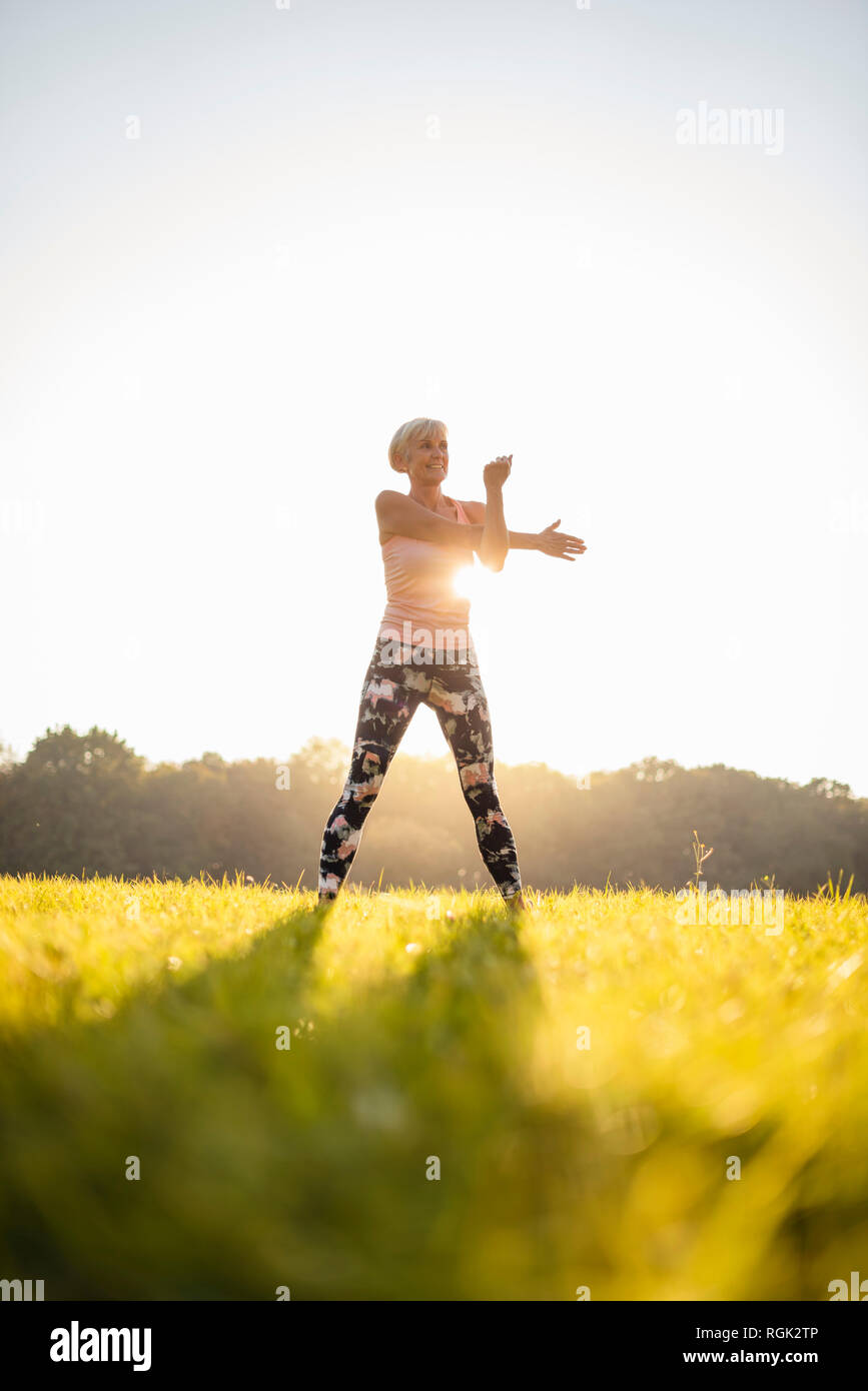 Senior woman stretching on rural meadow at sunset Stock Photo