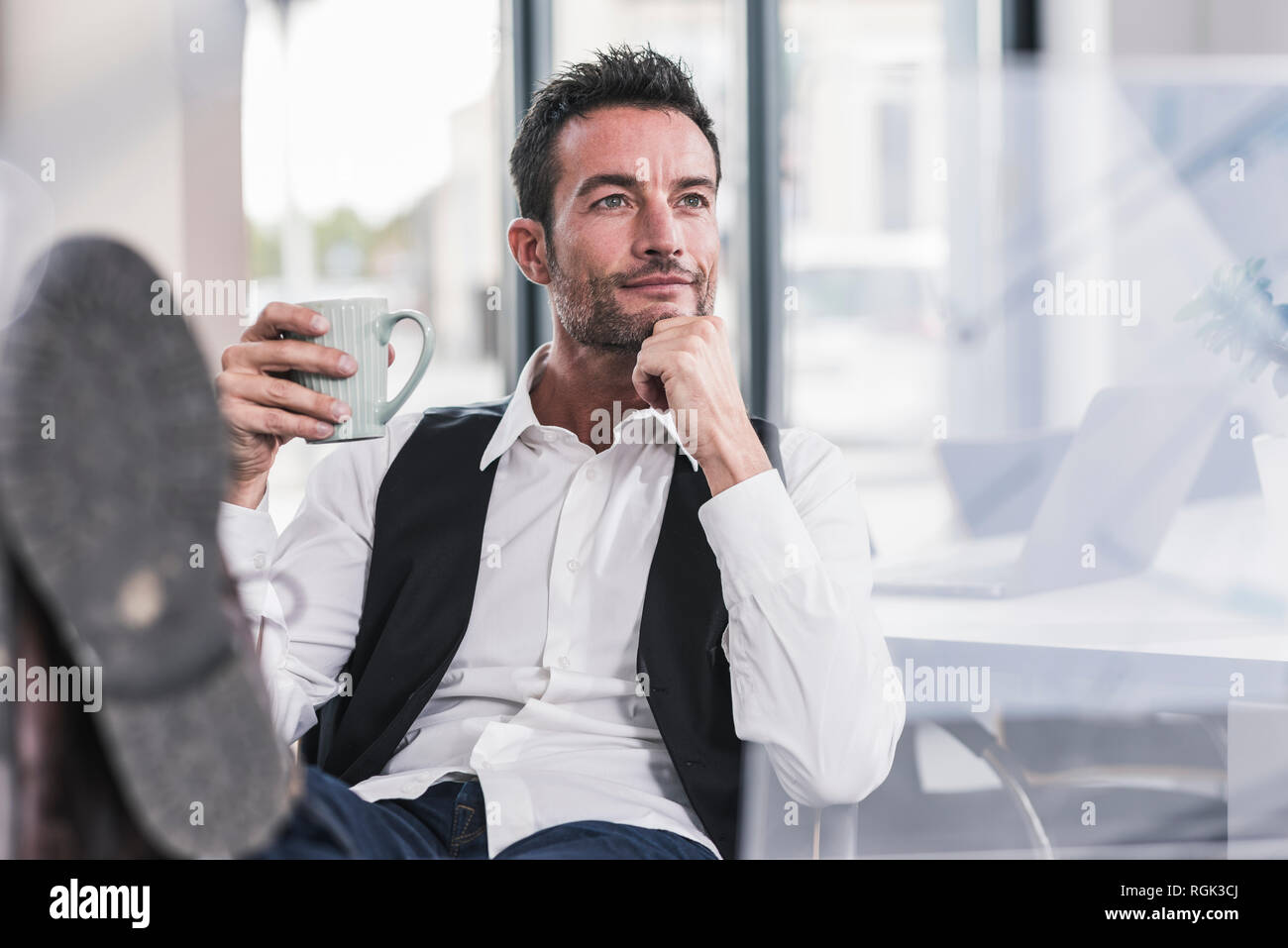 Businessman sitting in office, drinking coffee, with feet up Stock Photo