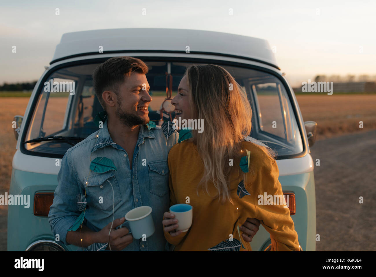 Happy young couple at camper van in rural landscape at sunset Stock Photo