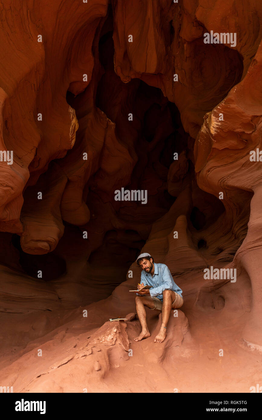 Young man sitting in a cave, taking notes Stock Photo
