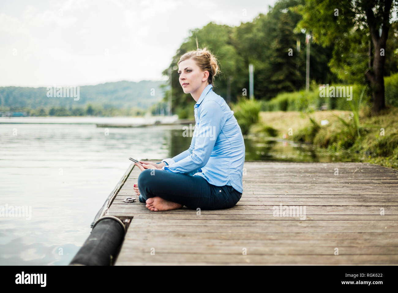 Woman sitting on jetty at a lake using tablet Stock Photo