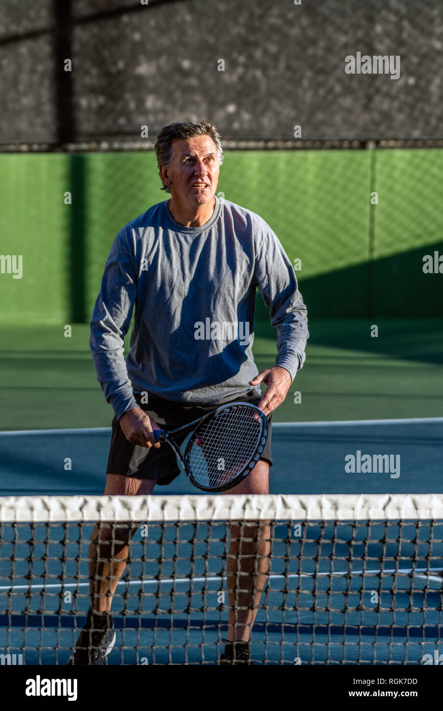 Focused and elderly recreational tennis player looking for opportunity to hit the ball during a game of tennis. Stock Photo