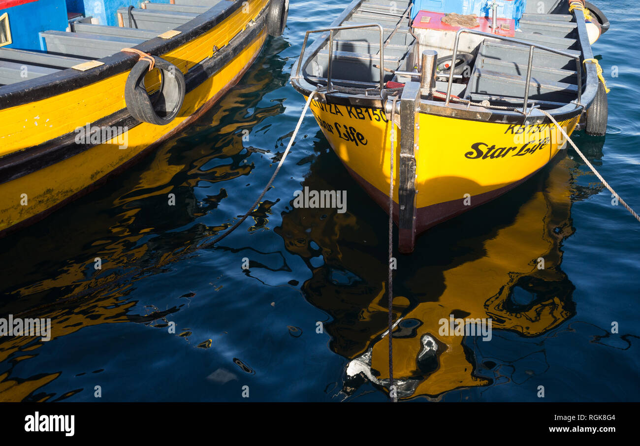 fishing and rowing boat, vibrant yellow with reflections in water and moored or tied up at Kalk Bay harbour, Cape Town, South Africa Stock Photo