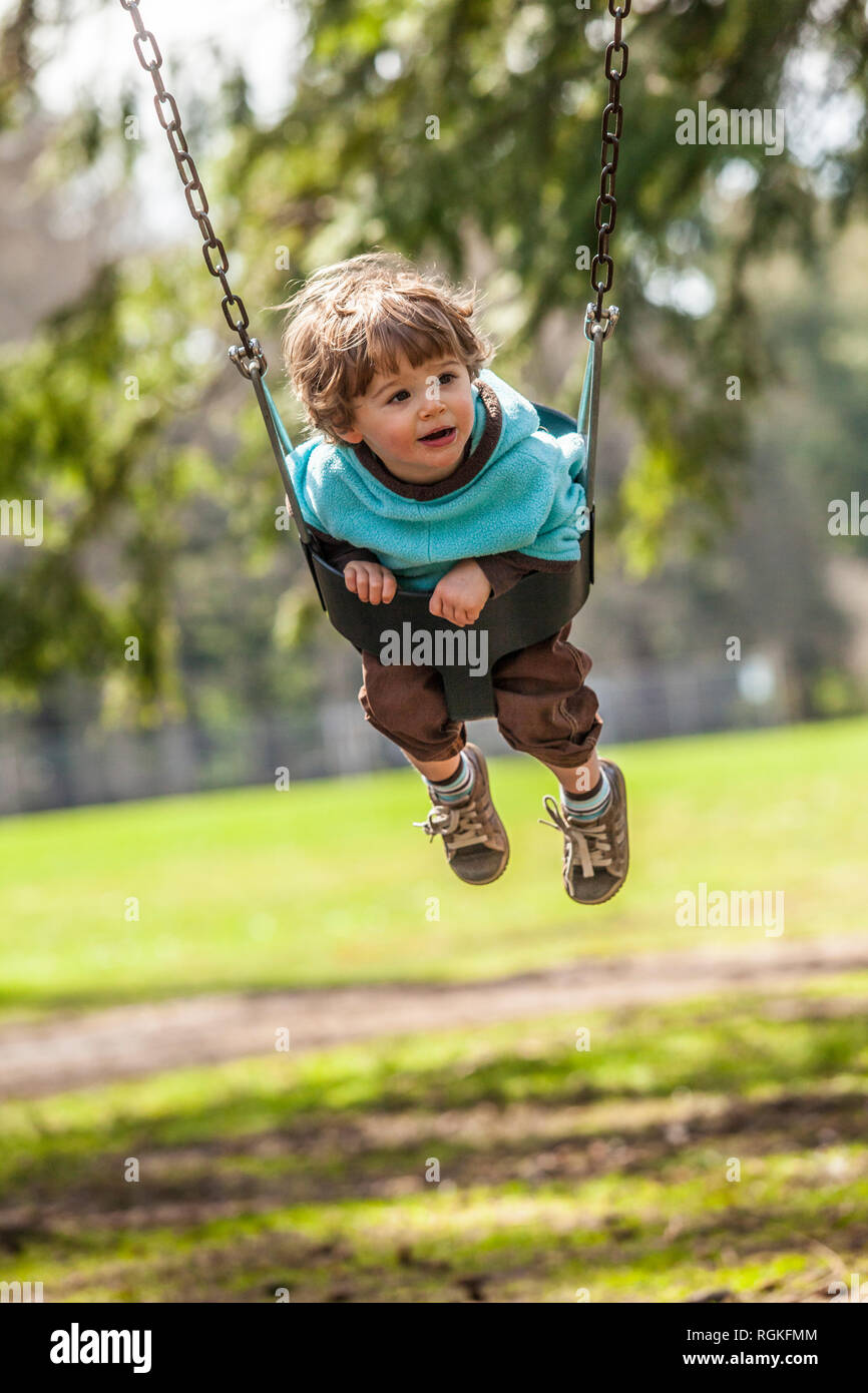 A toddler boy swinging in a swing in a park like setting Stock Photo