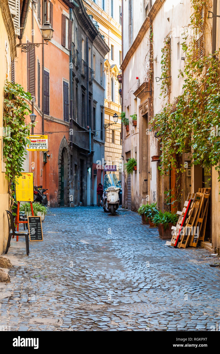 Rome, Italy - November 18, 2018: Cozy narrow ancient medieval Old Town  paving stone street with green overgrown facades, small businesses, parked  mope Stock Photo - Alamy
