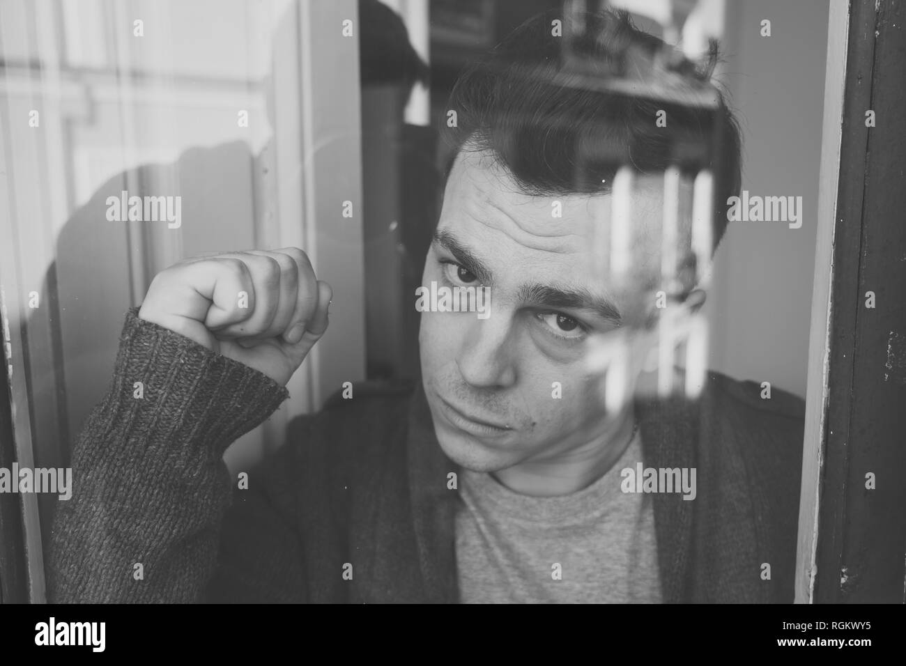 Close up portrait of young sad unhappy caucasian man looking worried, desperate and suicidal through the window at home. feeling worthless and in pain Stock Photo