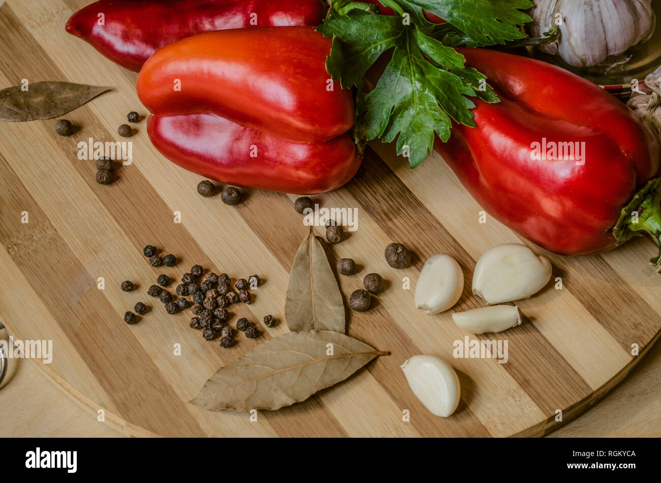 Bell red pepper with celery leaves, bay leaves,garlic and allspice lie on a wooden striped cutting board Stock Photo