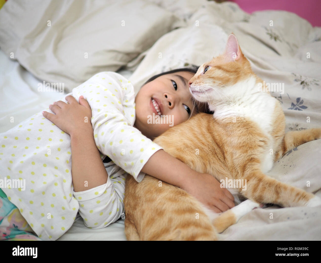 Kid hugging her orange tabby on the bed Stock Photo