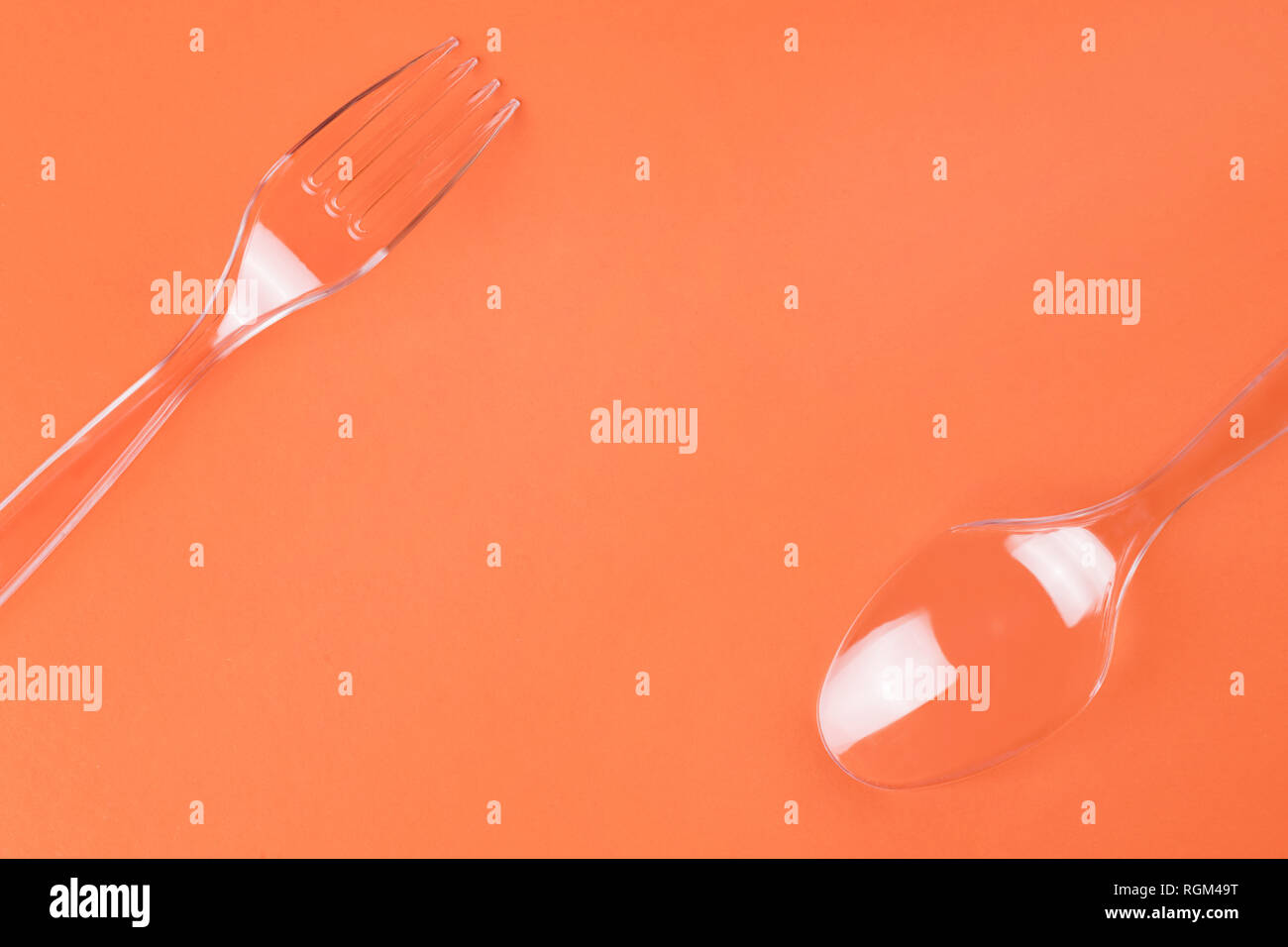 Transparent plastic fork and spoon on orange background top view with copy space Stock Photo