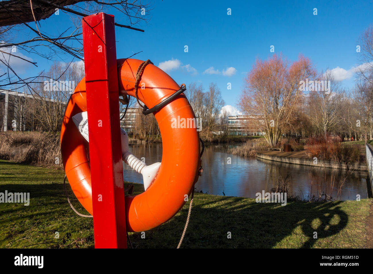 A bright orange life ring next to the waters edge by a lake in a business park. Stock Photo