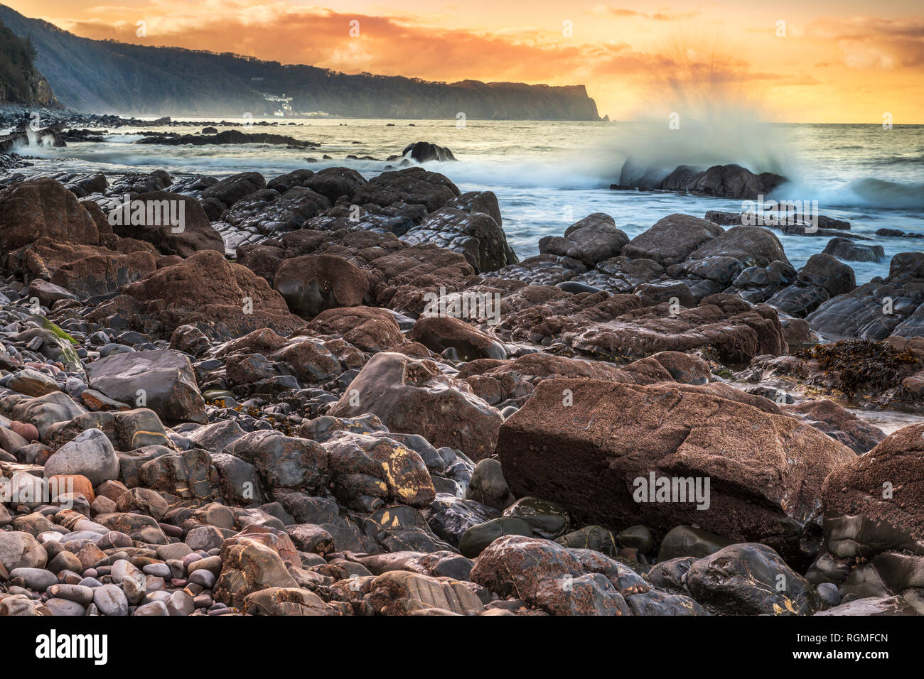 Bucks Mills, Devon, UK. 30th January 2019. After a cold overcast day in North Devon, the clouds finally part as the sun starts to set over the rocky shoreline at Bucks Mills. The seaspray from the incoming tide partially hides the distant white fishing village of Clovelly and Blackchurch Rock on the Hartland Peninsula. Credit: Terry Mathews/Alamy Live News Stock Photo