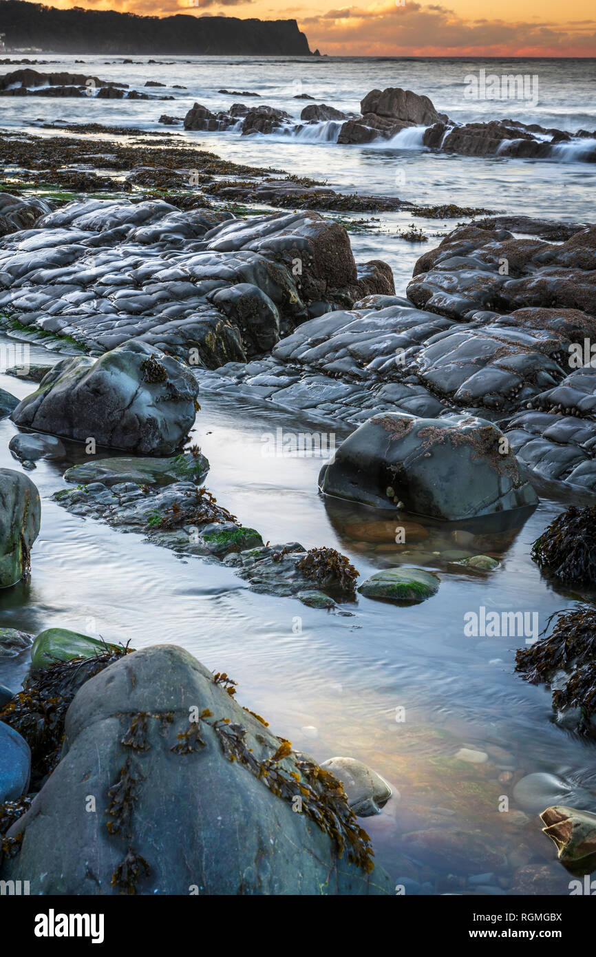 Bucks Mills, North Devon, UK. 30th Jan, 2019. UK Weather. After a cold overcast day in North Devon, the clouds finally part as the sun starts to set over the rocky shoreline at Bucks Mills. The seaspray from the incoming tide partially hides the distant white fishing village of Clovelly and Blackchurch Rock on the Hartland Peninsula. Credit: Terry Mathews/Alamy Live News Stock Photo