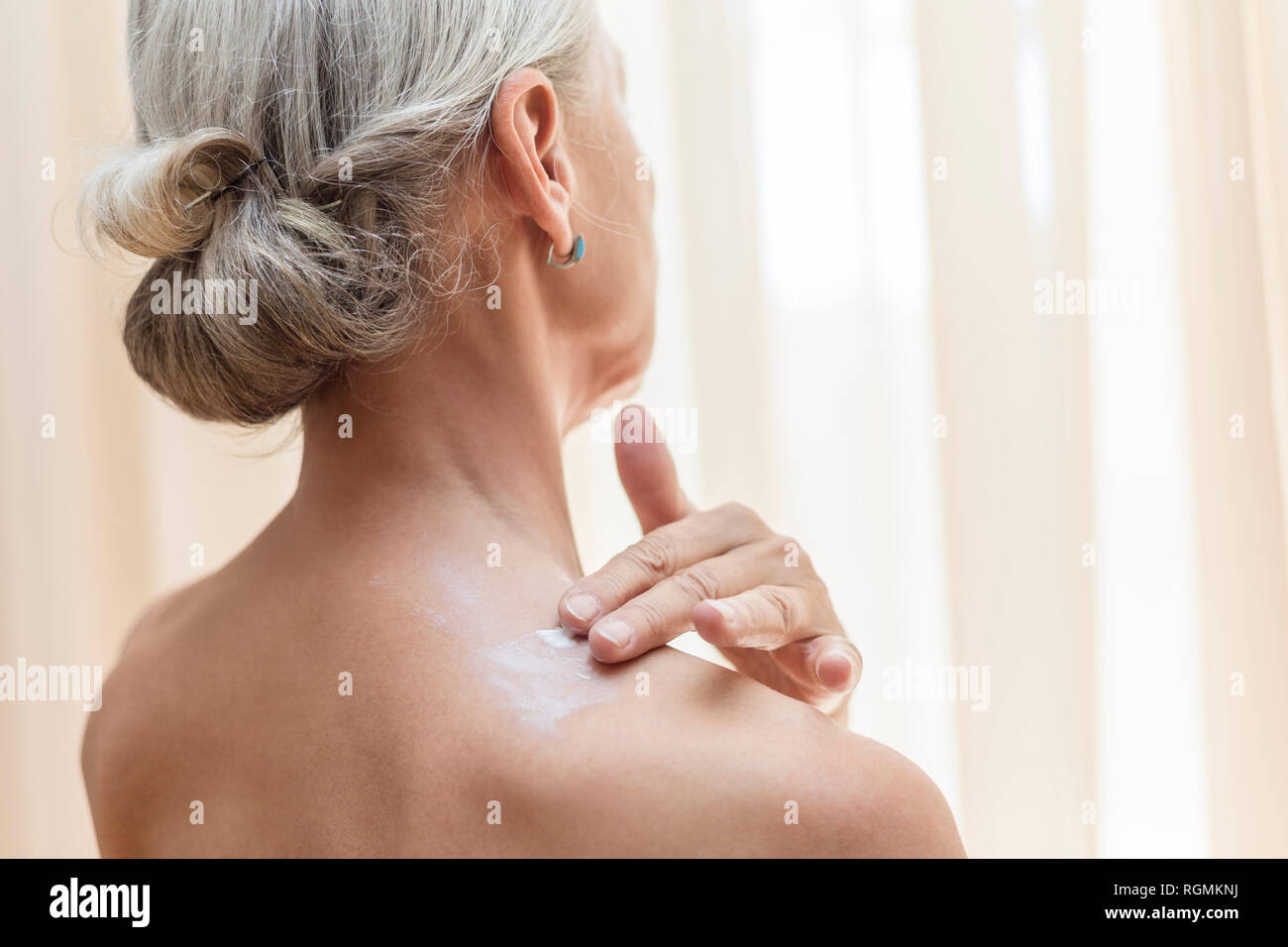 Back view of senior woman applying cream on neck Stock Photo