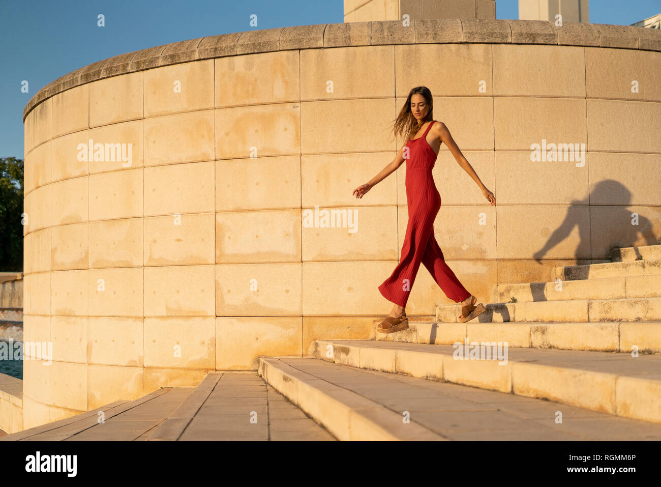 Spain, Barcelona, Montjuic, young woman wearing red jumpsuit walking on stairs Stock Photo