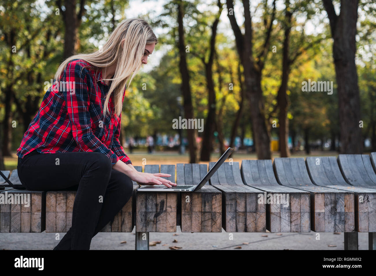 Young woman sitting on bench outdoors working on laptop Stock Photo