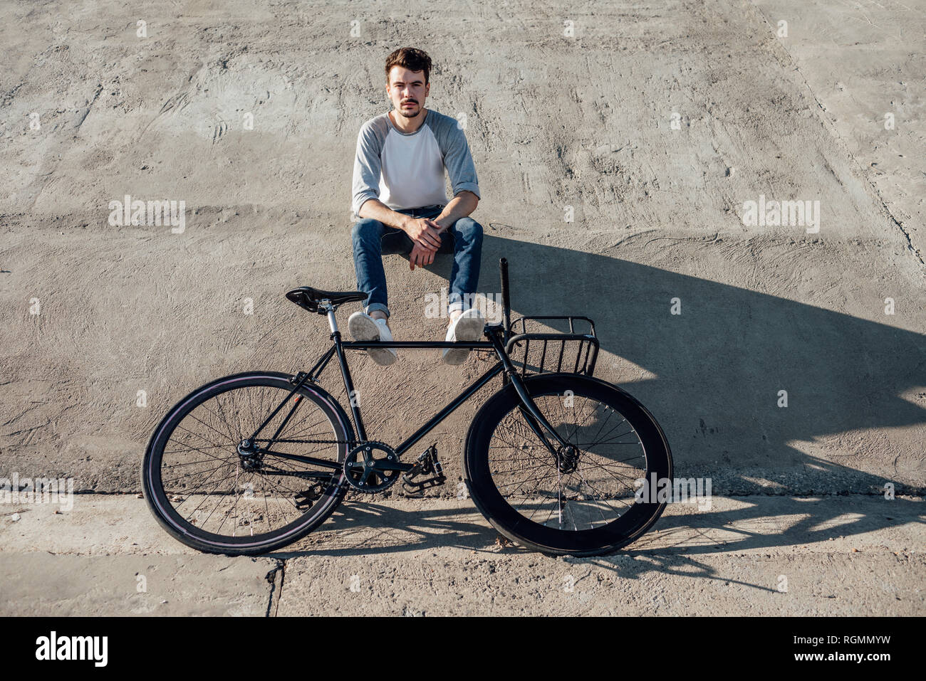 Young man with commuter fixie bike having a break sitting on concrete wall Stock Photo
