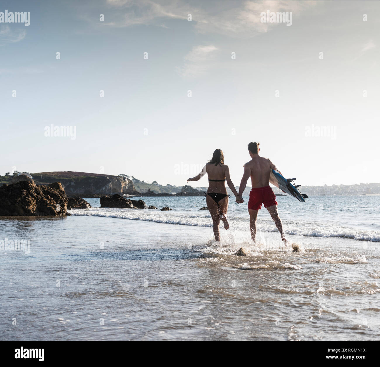 France, Brittany, young couple with surfboard running hand in hand in the sea Stock Photo