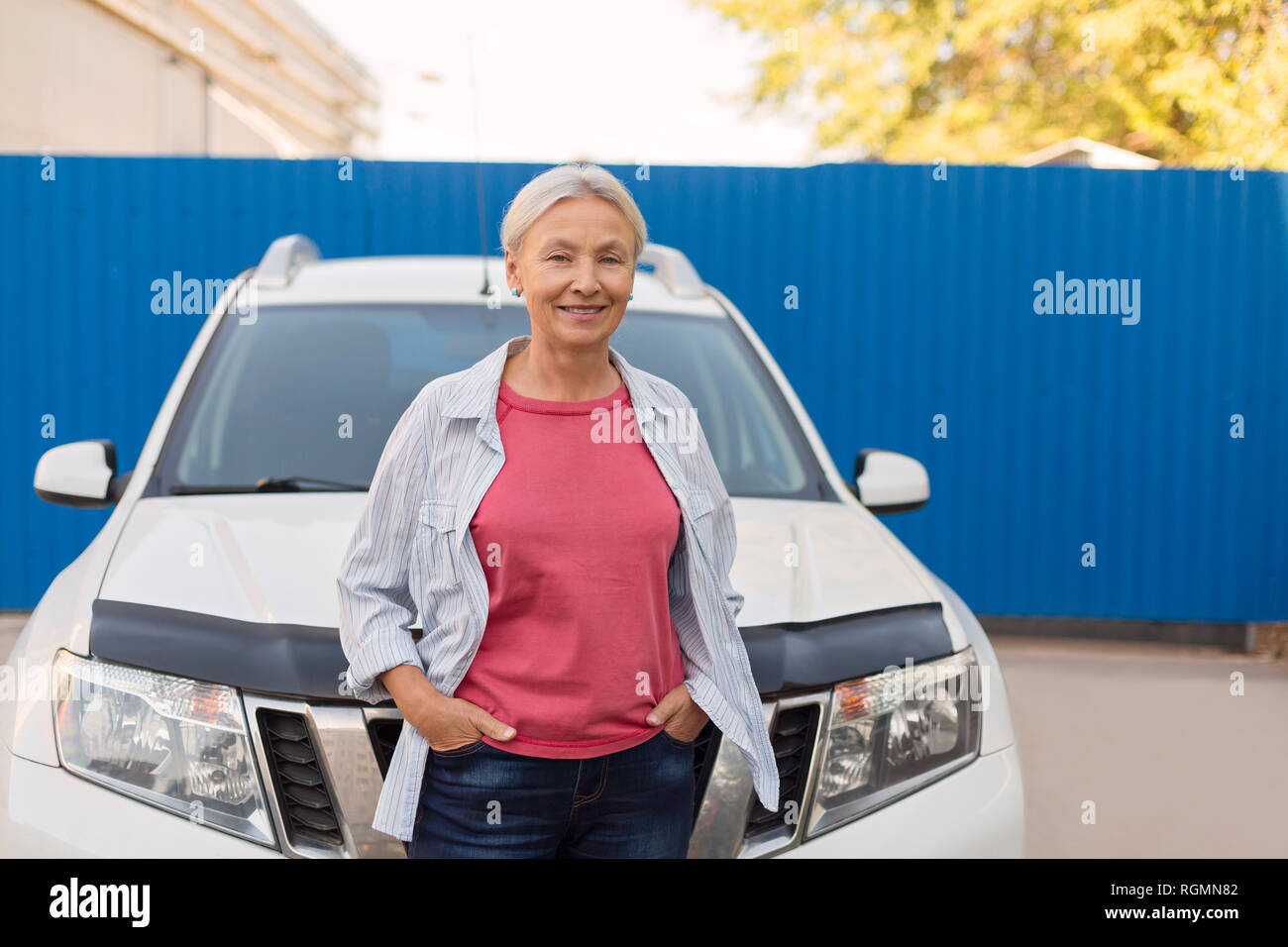 Portrait of smiling senior woman standing in front of her car Stock Photo