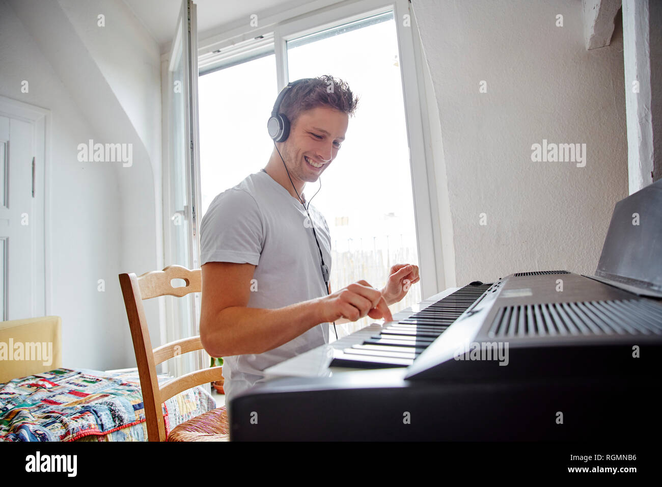 Smiling young man at home wearing headphones playing digital piano Stock Photo