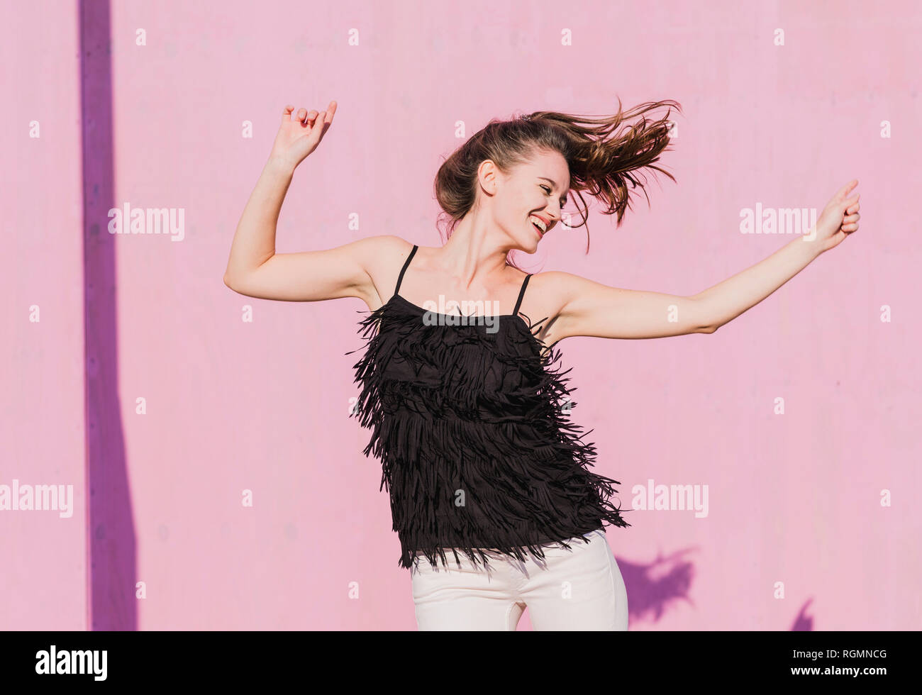 Happy young woman moving in front of pink wall Stock Photo - Alamy