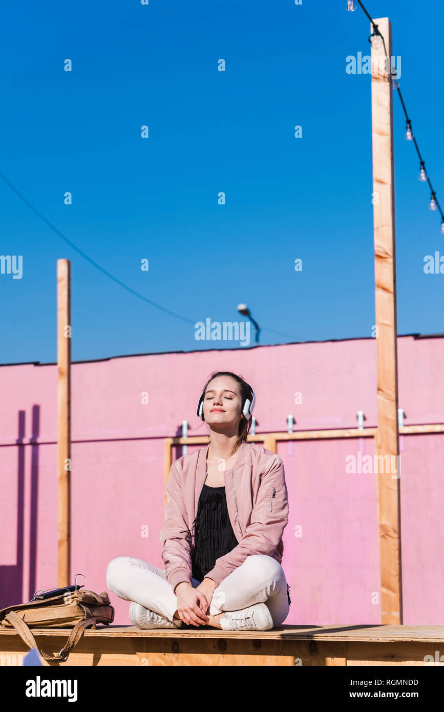 Relaxed young woman sitting on platform listening to music Stock Photo