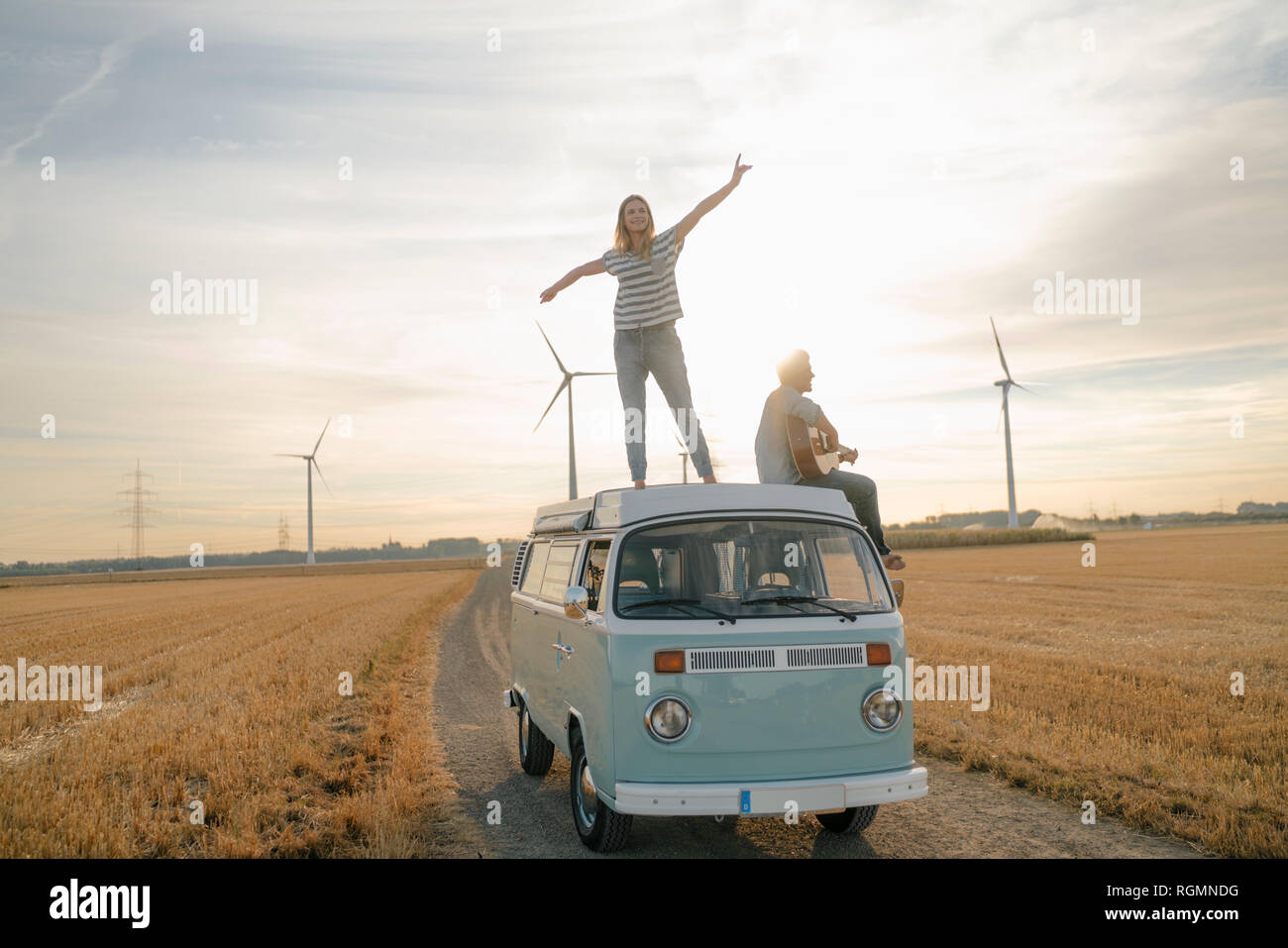 Happy couple with guitar on roof of a camper van in rural landscape ...