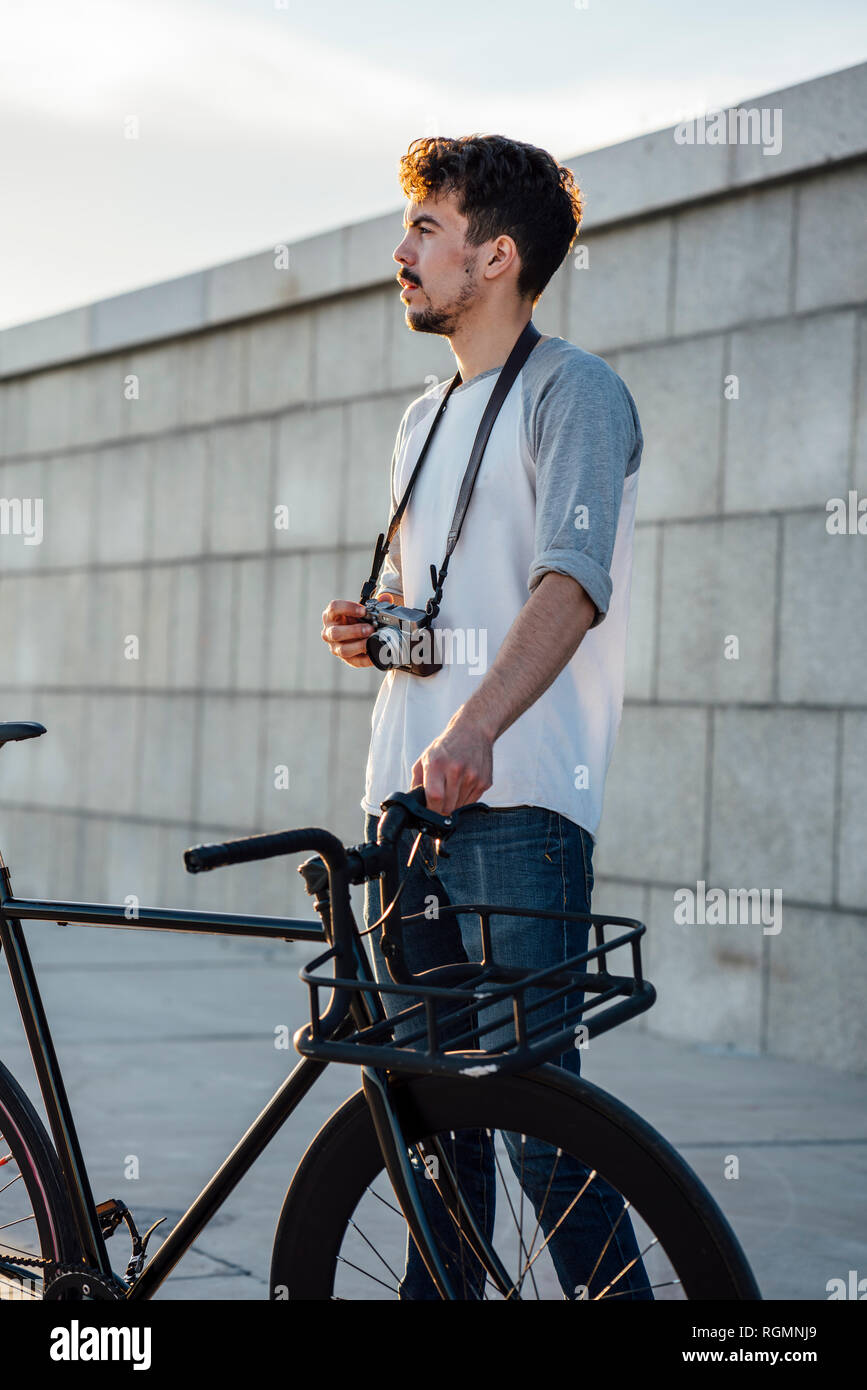 Young man with commuter fixie bike and camera looking around Stock Photo