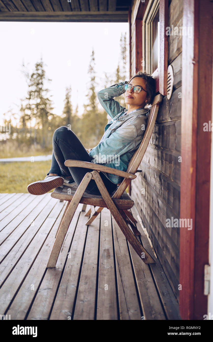 Sweden, Lapland, portrait of young woman sitting on chair on veranda relaxing Stock Photo