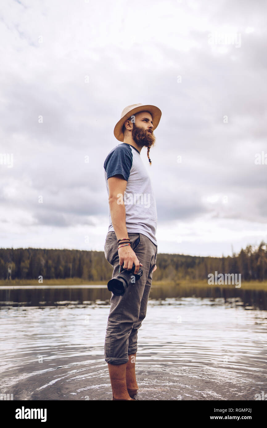 Sweden, Lapland, man with camera standing in water looking at distance Stock Photo