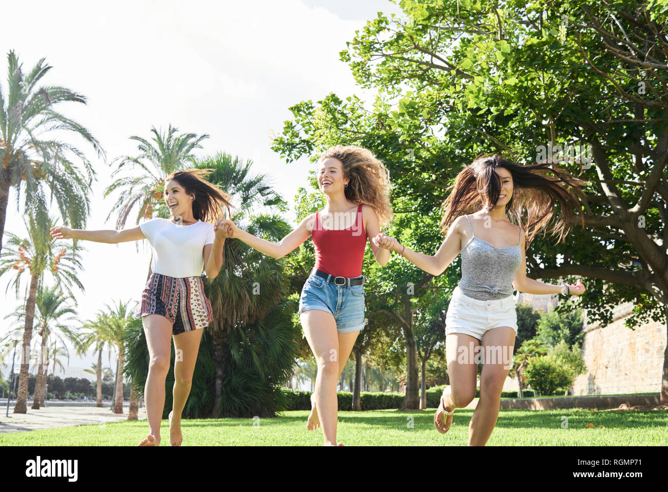 Spain, Mallorca, Palma, three happy young running holding hands together in a park in summer Stock Photo