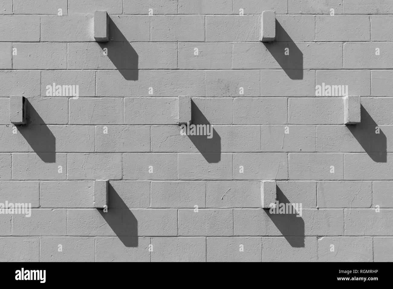 Bricks that are protruding from a cinder block wall are casting diagonal shadows. The scene looks similar to the face of a clock. Stock Photo