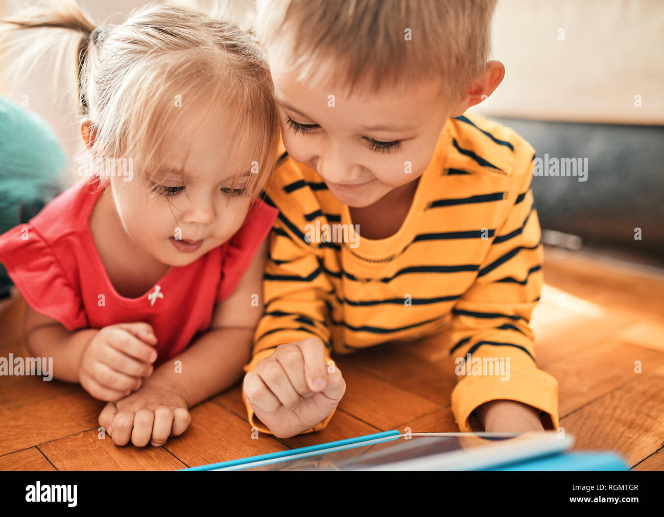 Brother and little sister lying on the floor at home using digital ...