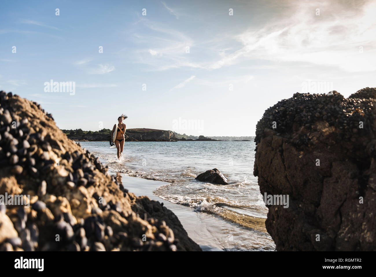 France, Brittany, young woman carrying surfboard running in the sea Stock Photo