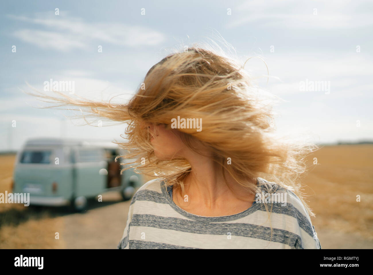 Blong young woman at camper van in rural landscape shaking her hair Stock Photo