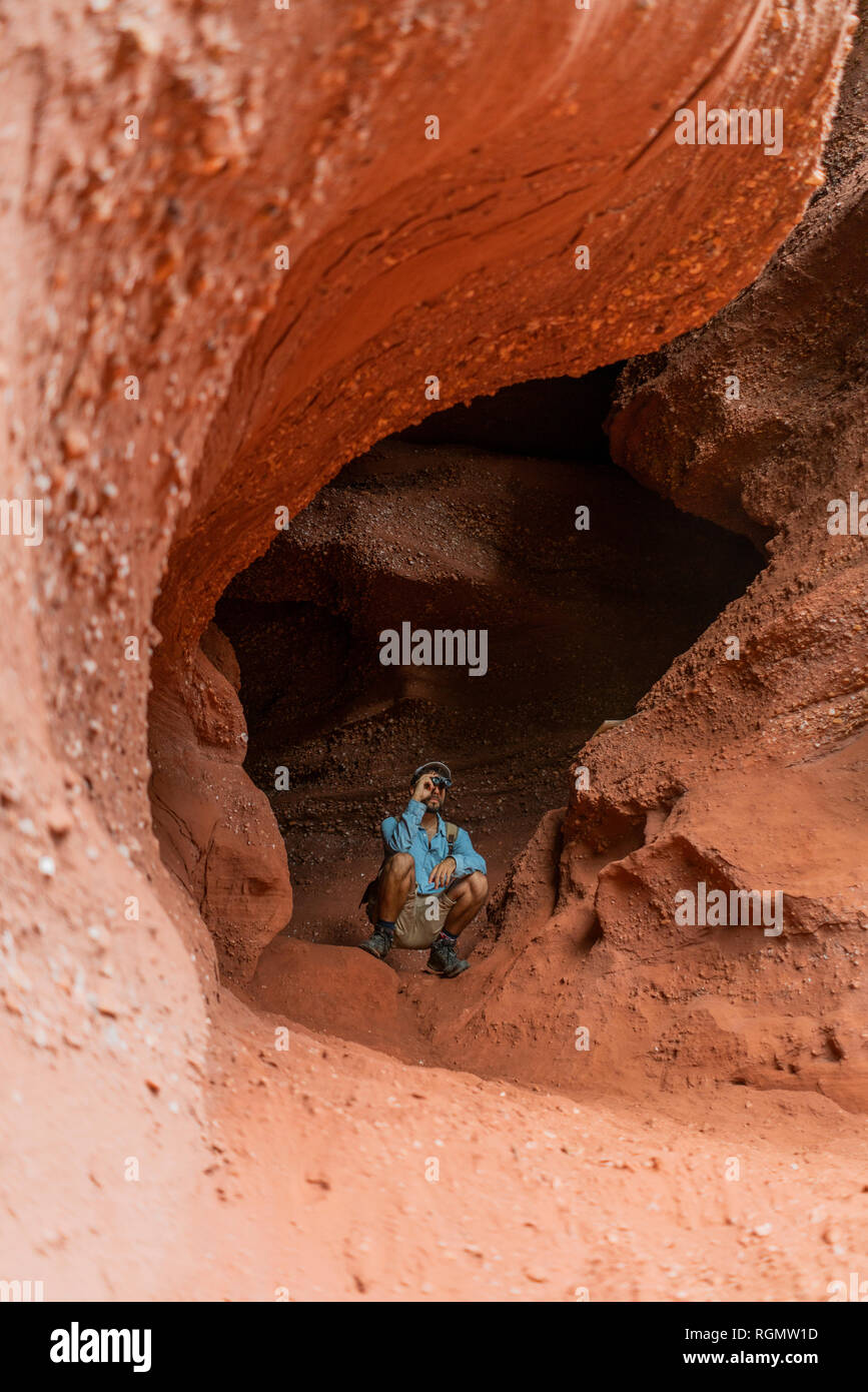 Young man sitting in a cave, looking through binoculars Stock Photo