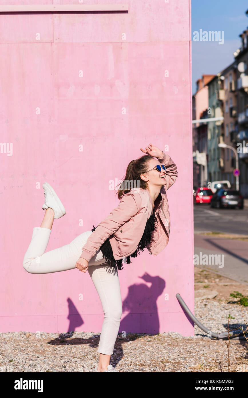 Happy young woman moving in front of pink wall Stock Photo