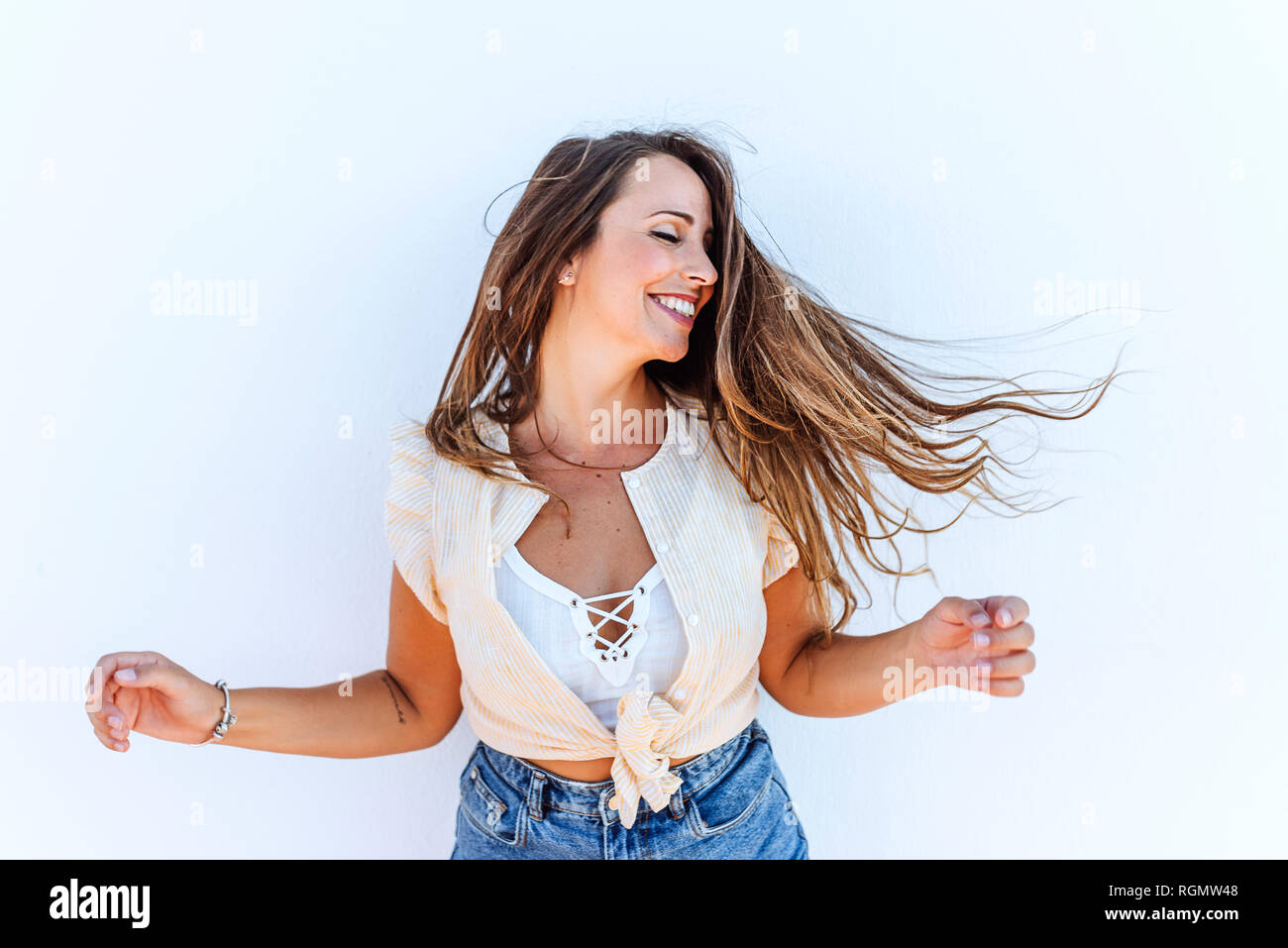 Happy young woman shaking her hair in front of white wall Stock Photo