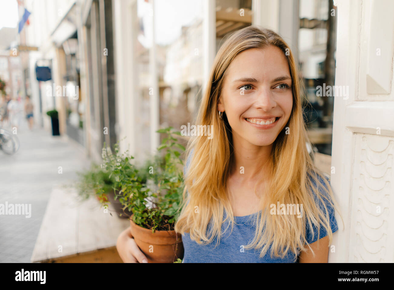 Netherlands, Maastricht, smiling blond young woman holding flowerpot in the city Stock Photo