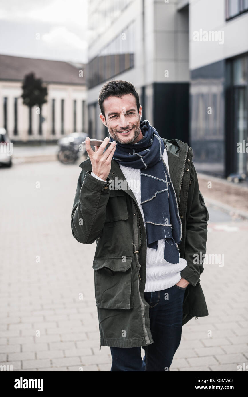 Mature man, wearing coat and scarf, walking in the city, talking on the phone Stock Photo