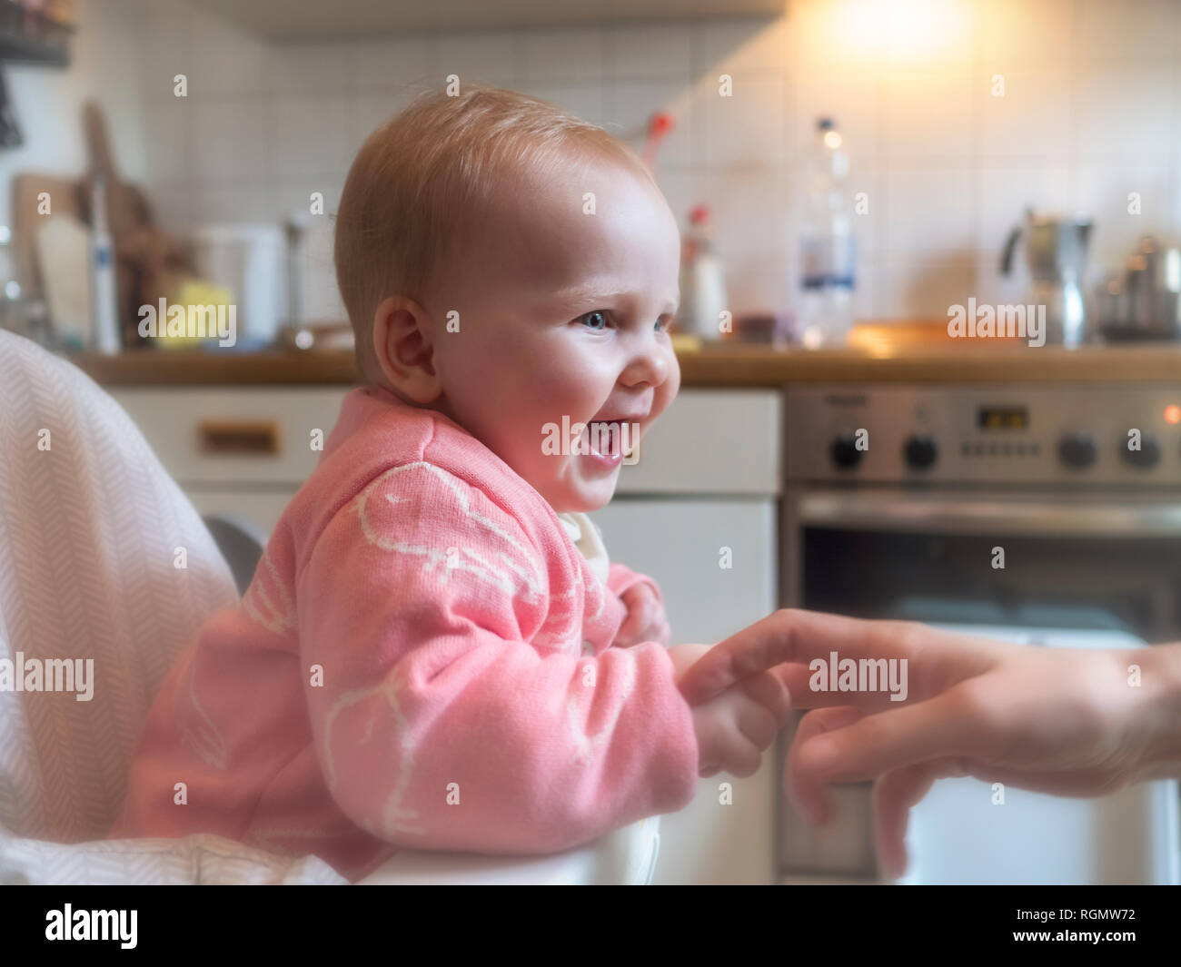 Happy baby girl in sitting in high chair in kitchen Stock Photo