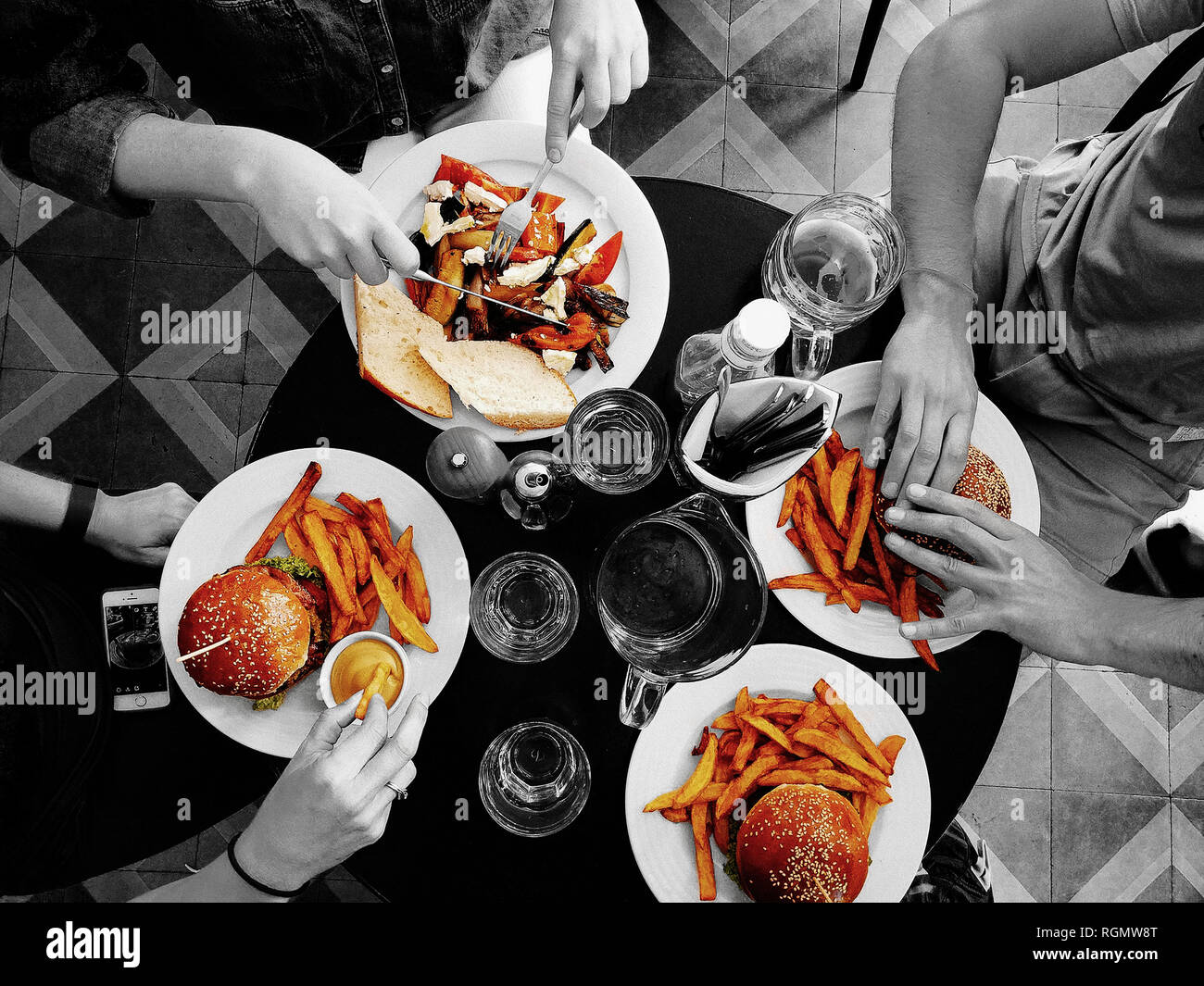 A monochrome photo with the food and meal in color. Top view of people dining on a table and holding food. Stock Photo