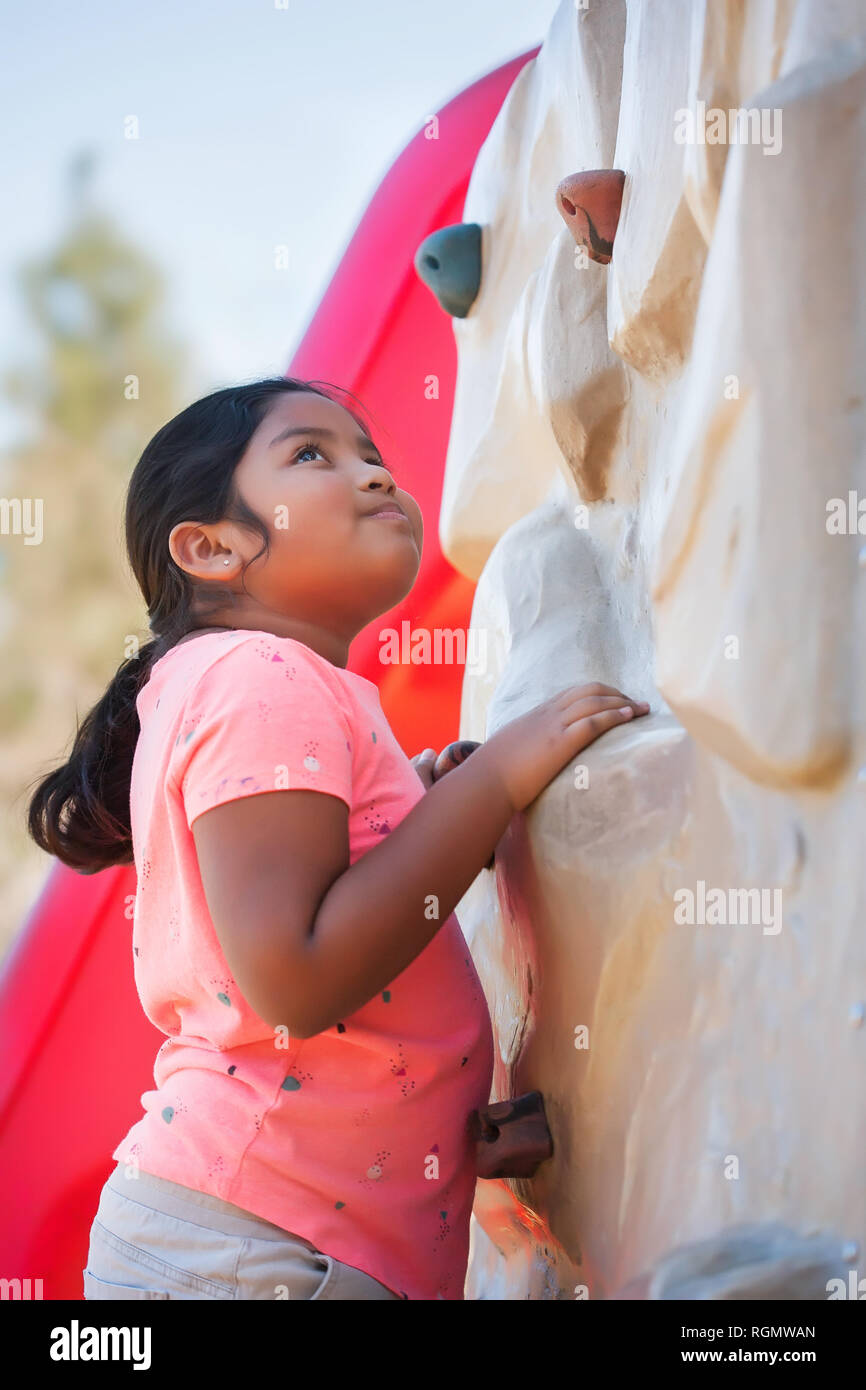 Girl standing in front of a climbing wall looking up with a thoughtful expression on face. Stock Photo