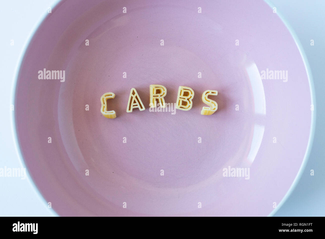 The word 'carbs' composed with real pasta letters in a pink dish. Stock Photo