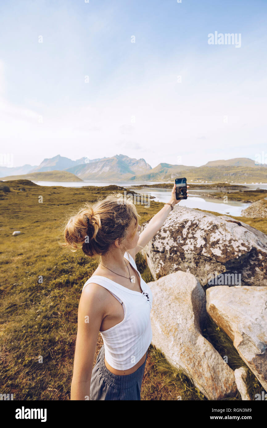 Norway, Lofoten, young woman taking selfie with smartphone in nature Stock Photo