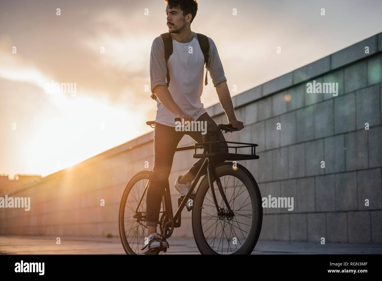 Young man with backpack riding bike on promenade at sunset Stock Photo