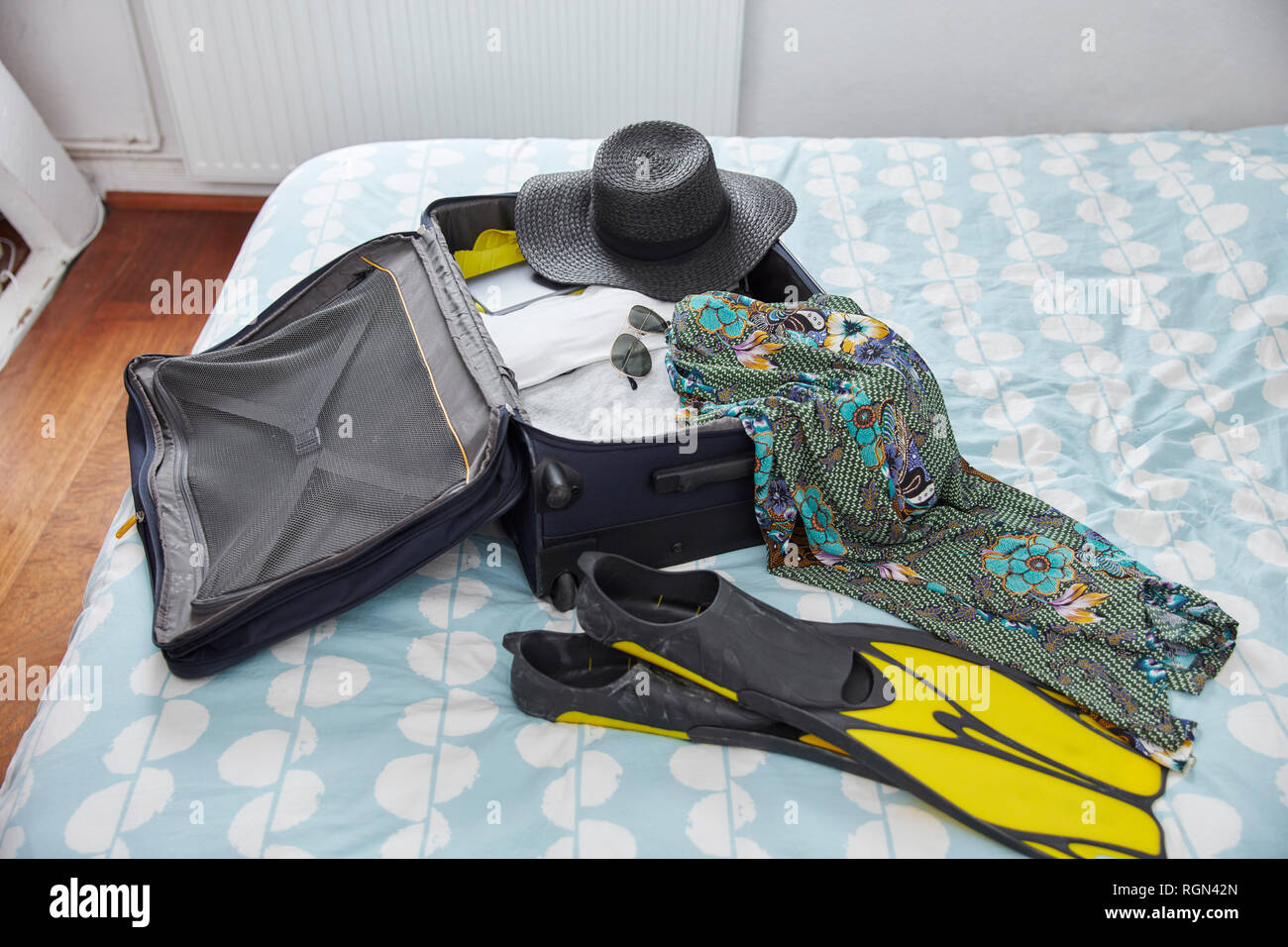 Suitcase with summer vacation utensils on bed Stock Photo