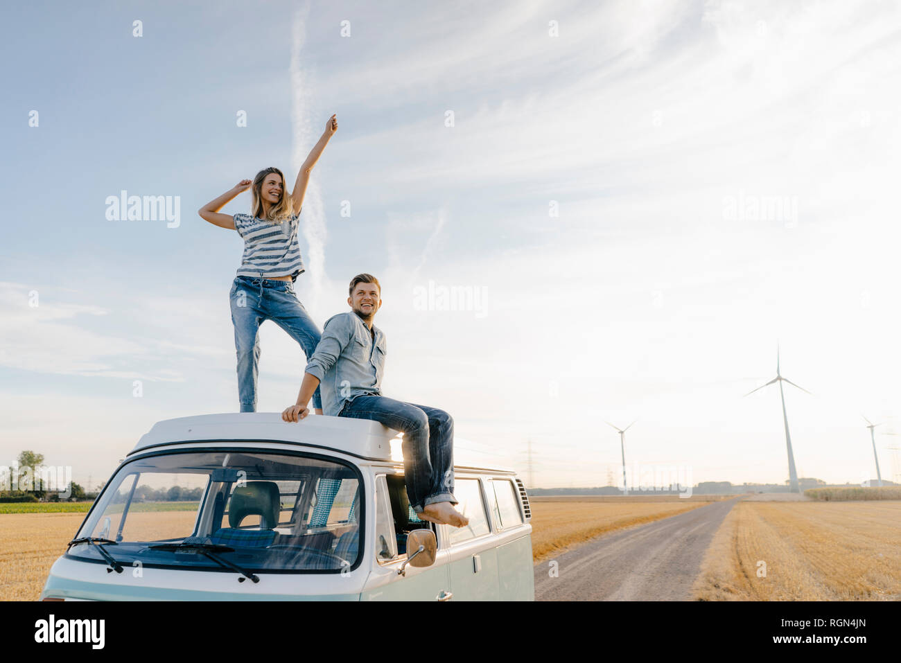 Happy couple on roof of a camper van in rural landscape Stock Photo