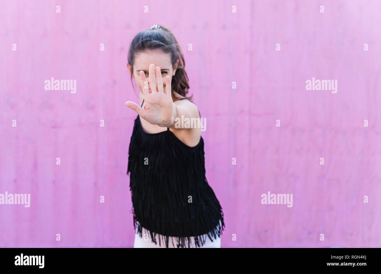 Young woman standing in front of pink wall raising her hand Stock Photo